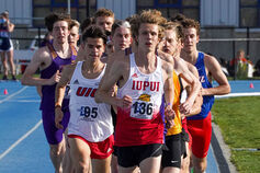 A group of male track and field athletes running on the track with an IUPUI student in the lead.